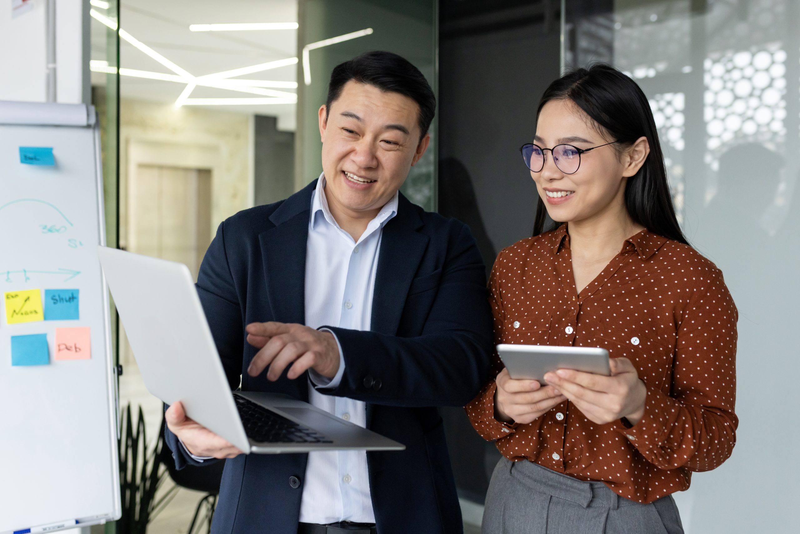 Asian business professionals collaborating on project with laptop and tablet in modern office setting