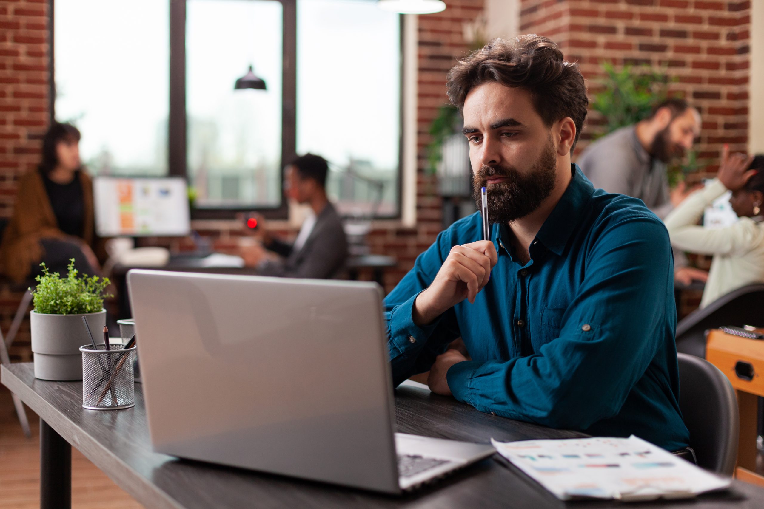 Doubtful pensive entrepreneur having uncertain think about marketing project analyzing company turnover on computer. Businessman working at business collaboration in startup office. Diverse team - self-aware man.